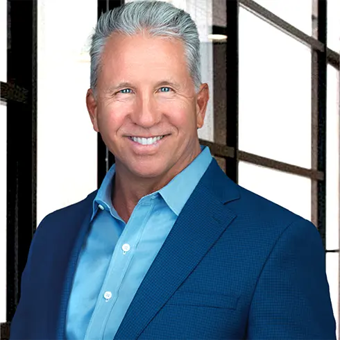 Professional headshot of Bill Bergau, ACC Executive Coach and certified emotional intelligence trainer, smiling in a blue suit with a modern office background.